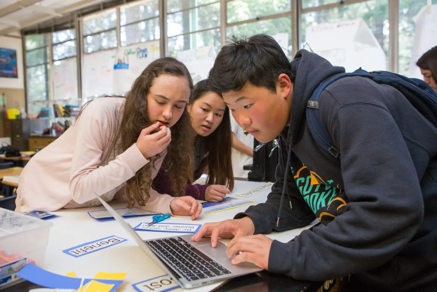 Three high school students lean in over a laptop to finish a class project